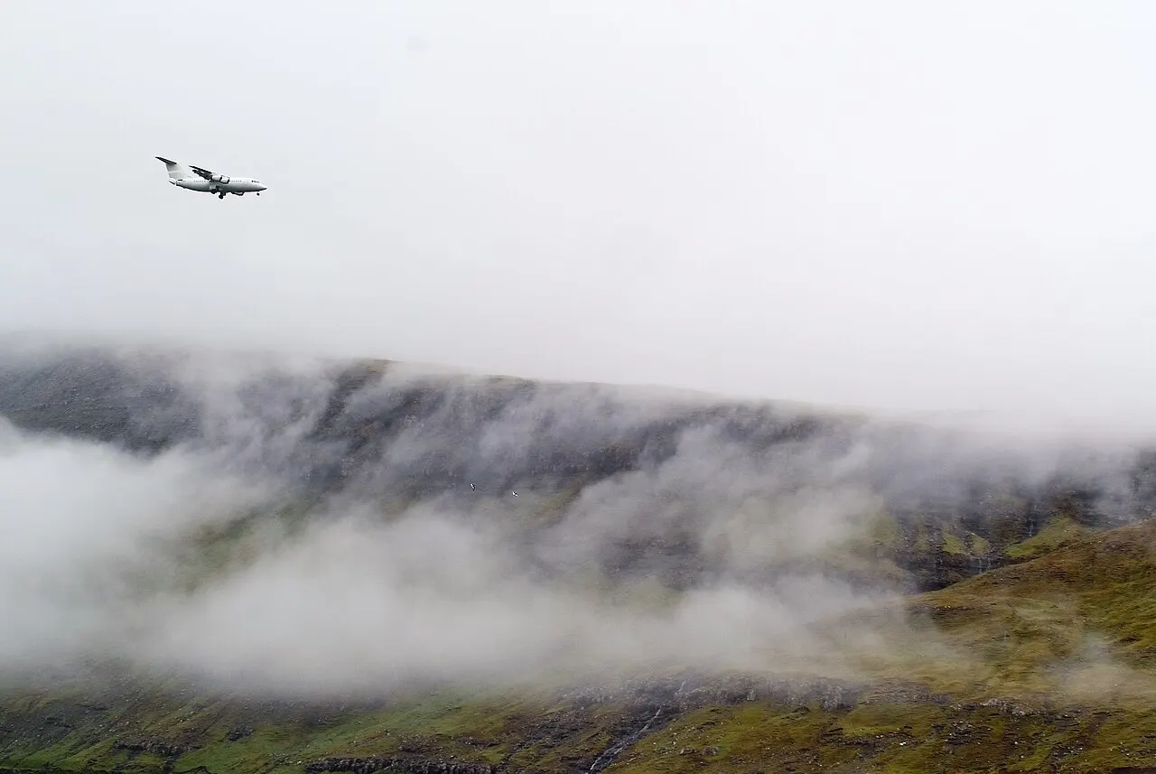 Um avião em aproximação entre a névoa e as montanhas