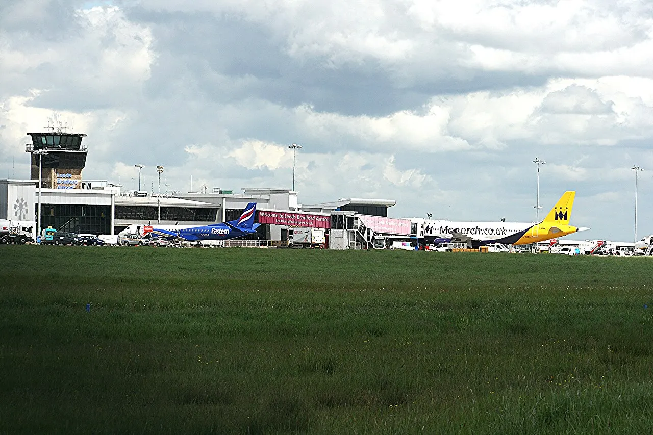 Aircraft and the terminal with its control tower, seen across the grass beside the runway