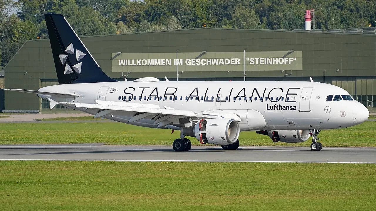 An Airbus A319 on the runway, with an air base hangar behind